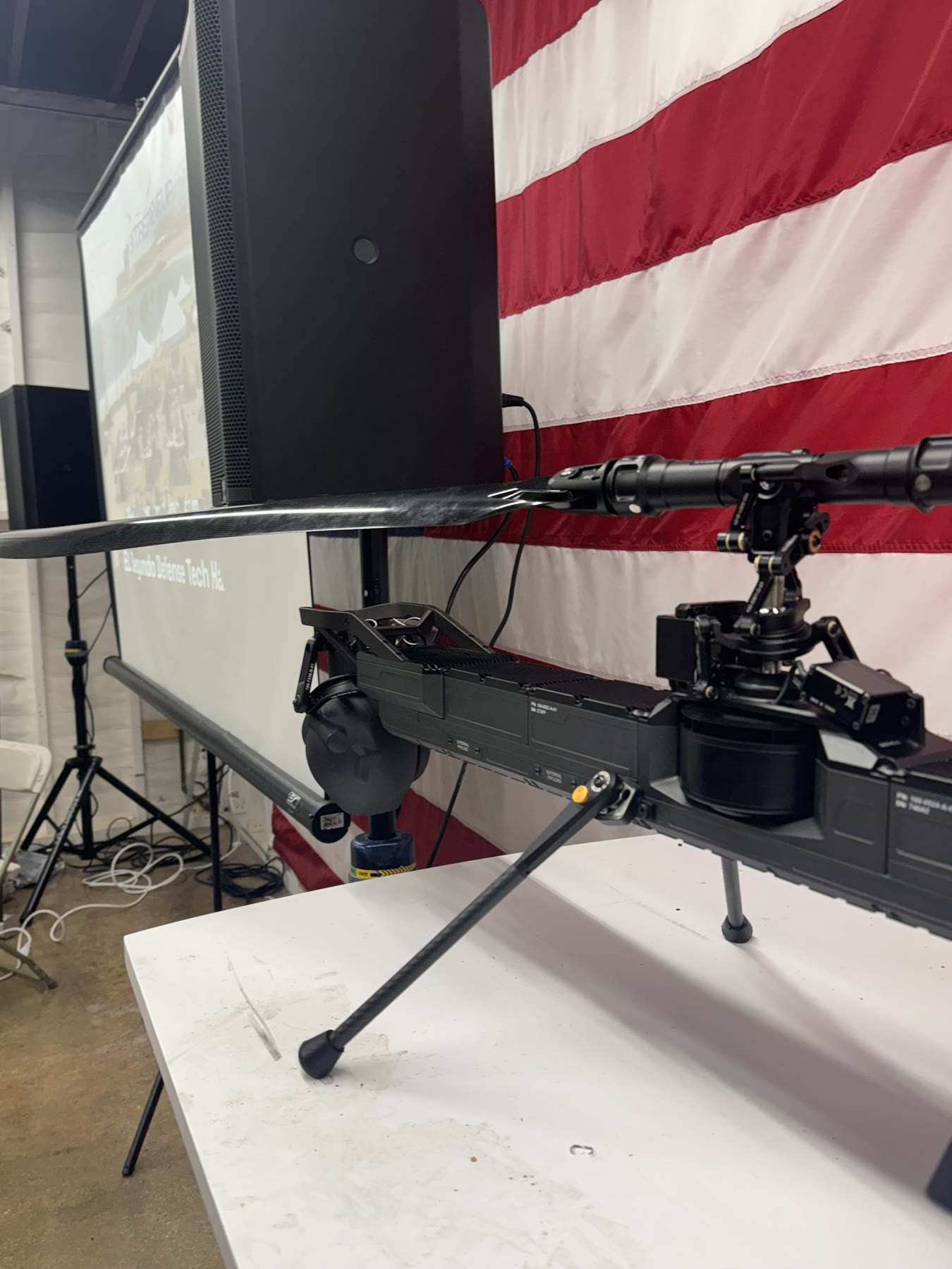 Black unmanned aerial vehicle with a carbon-fiber rotor displayed in front of a United States flag