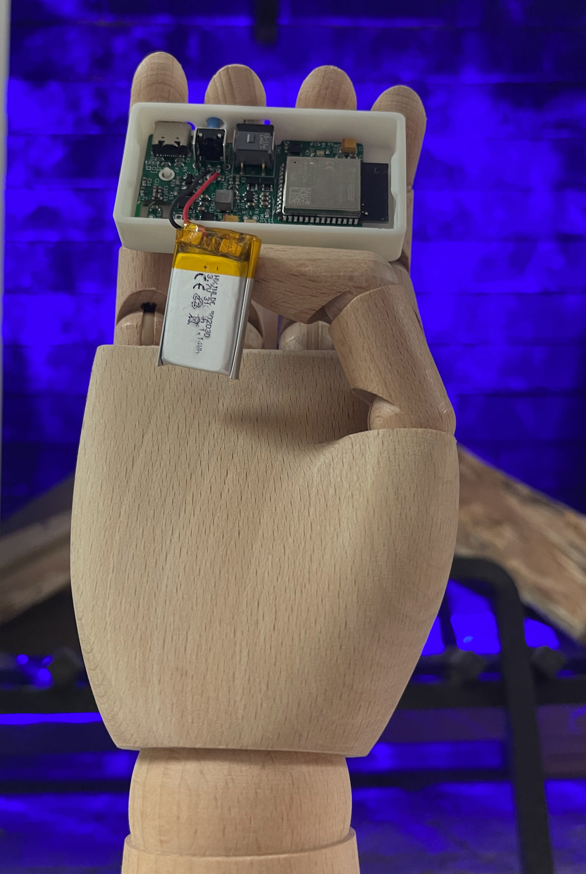 Completed ESP32-based BCI circuit board and battery held by a wooden articulated hand